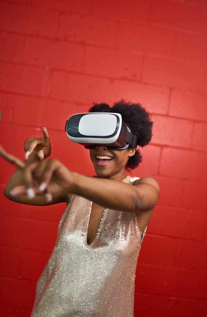 A Black woman dancing with digital glasses with a wall made of red bricks
