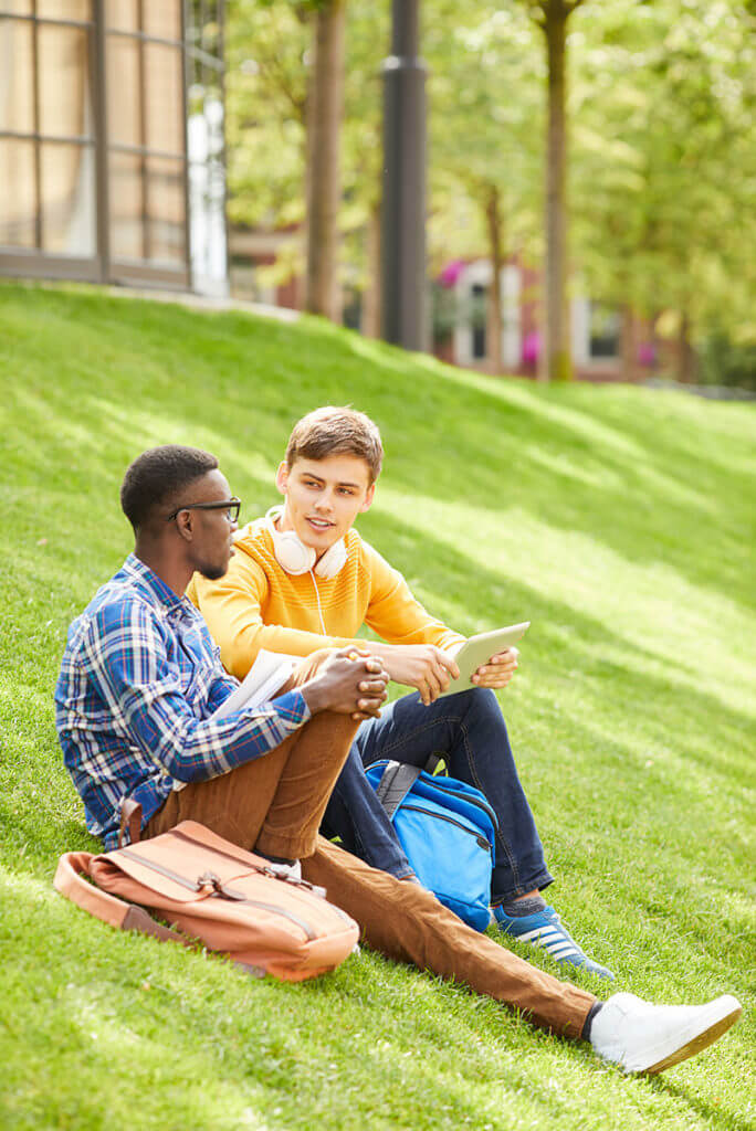Two students sitting on the grass chatting about their assignments