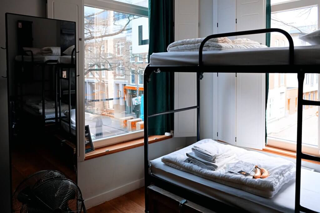 A dorm room with 2 big windows and a bunk bed