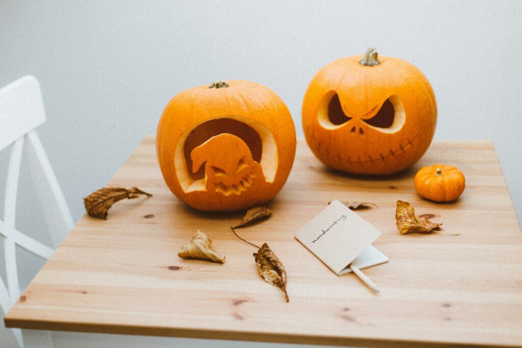 Two Carved Pumpkins and Autumn Leaves on a Wooden Table