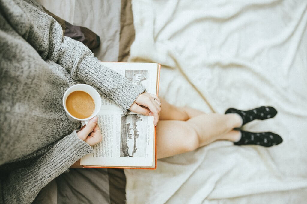 A girl sitting with an old book on her legs while she has a cup of coffee
