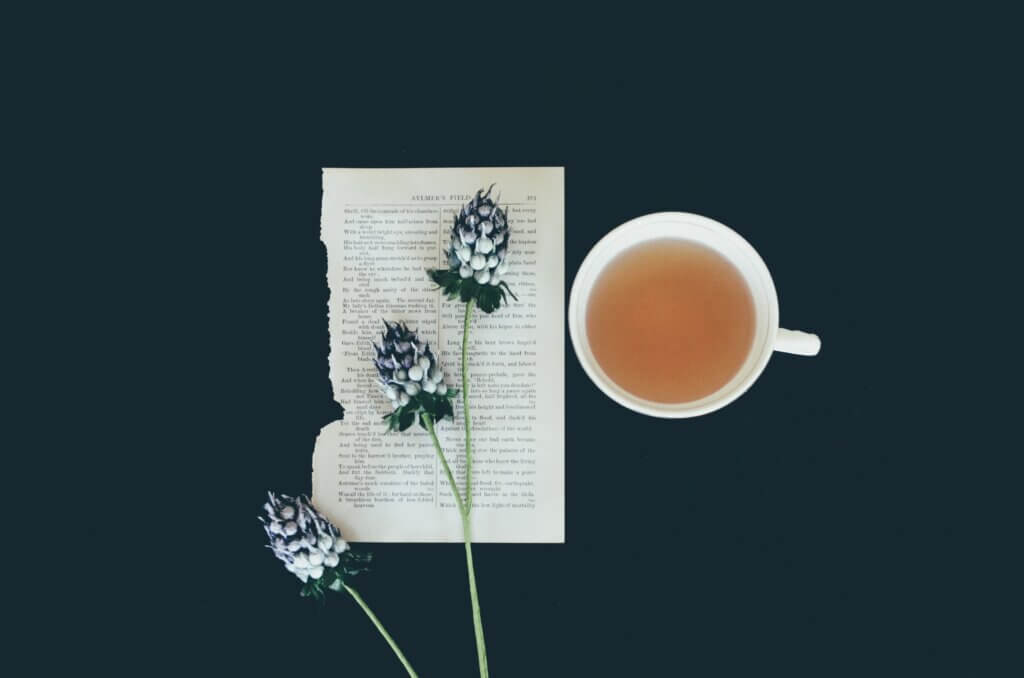 Image of a cup of tea next to a bit of writing that's ready to be read with flowers on top