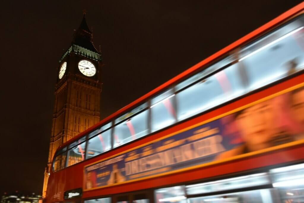 A view from the ground of Big Ben by night with a London red bus driving by