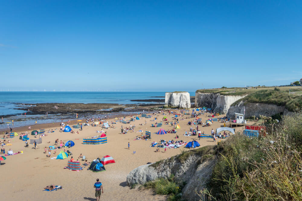Botany Bay view on a sunny day with a lot of people on the sandy beach and white cliffs behind the beach
