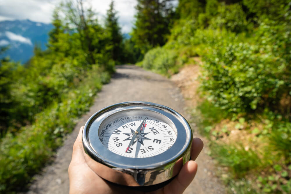 A hand holding a compass on a mountain trail