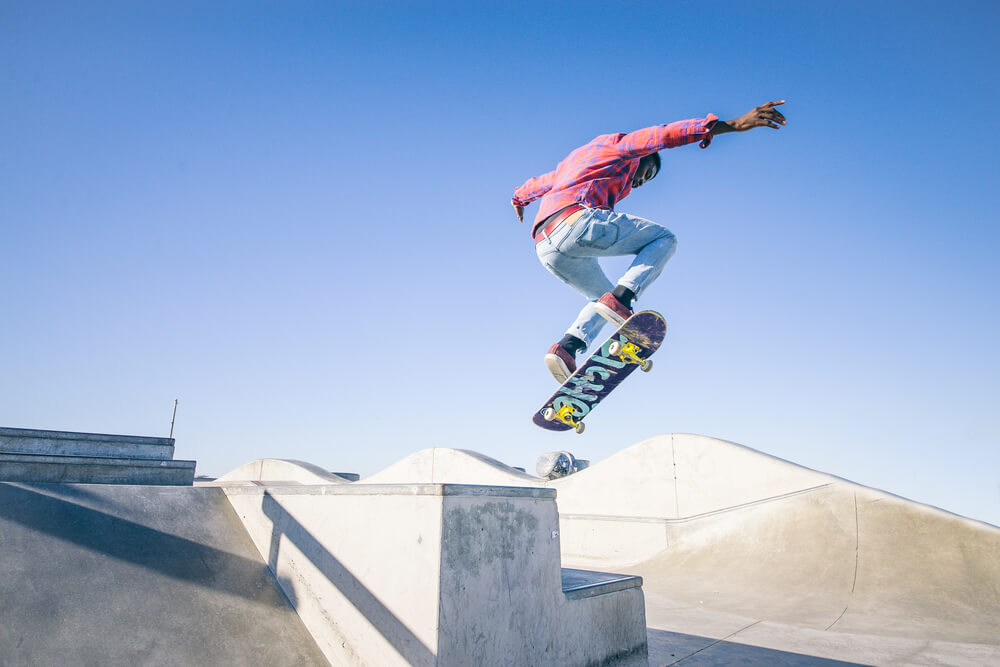 A young boy wearing a pink jumper is jumping with his skateboard