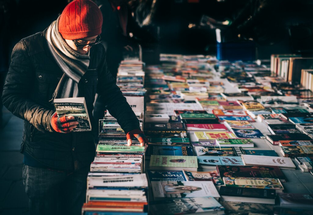 Person at a market picking up books with a red winter hat on and fingerless gloves