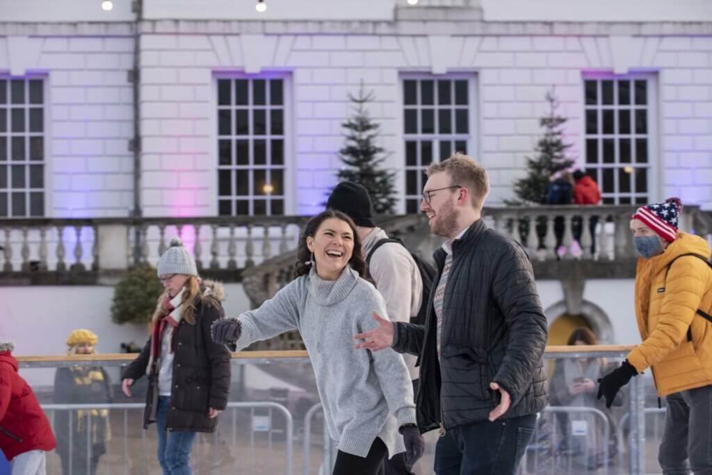A couple ice skating and laughing together at a London ice rink