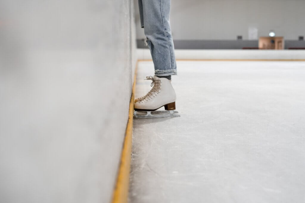Someone stood against the wall in an ice rink wearing ice skates